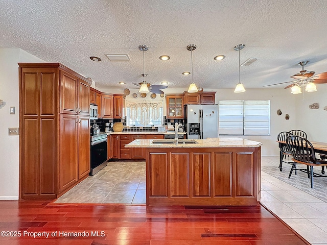 kitchen with sink, pendant lighting, stainless steel appliances, and an island with sink