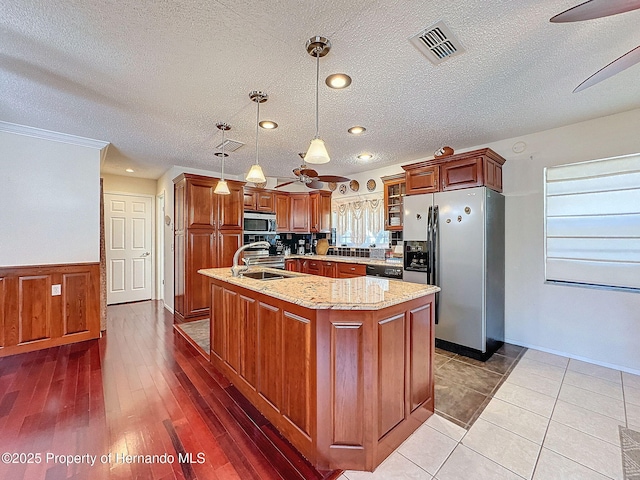 kitchen with light stone countertops, pendant lighting, appliances with stainless steel finishes, an island with sink, and sink