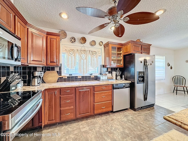 kitchen featuring a textured ceiling, appliances with stainless steel finishes, backsplash, ceiling fan, and light stone counters