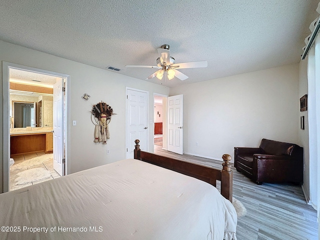 bedroom with ceiling fan, ensuite bathroom, a textured ceiling, and light hardwood / wood-style flooring