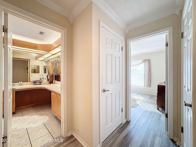 hallway with a textured ceiling, crown molding, and light wood-type flooring