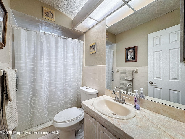 bathroom featuring a textured ceiling, tile patterned flooring, vanity, tile walls, and toilet