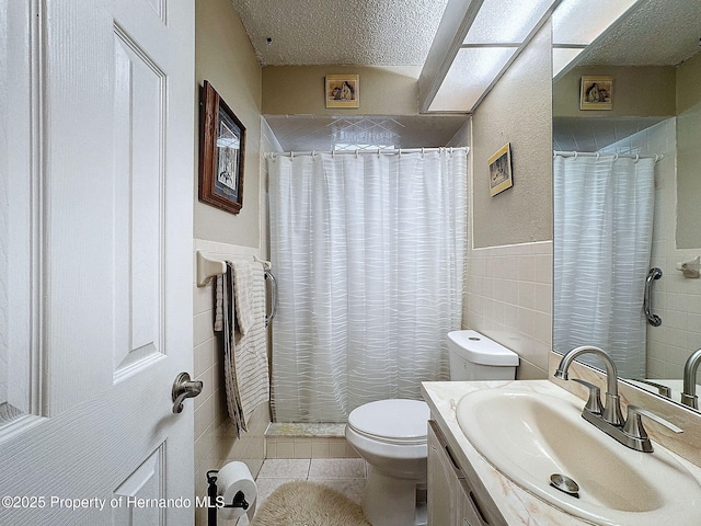 bathroom with toilet, tile patterned flooring, tile walls, a textured ceiling, and vanity