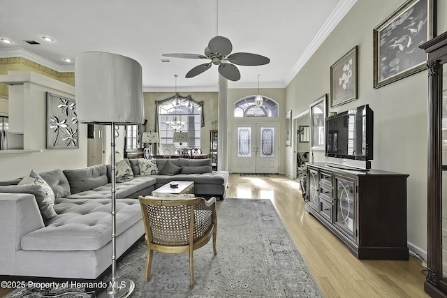 living room with ceiling fan with notable chandelier, light hardwood / wood-style flooring, crown molding, and french doors