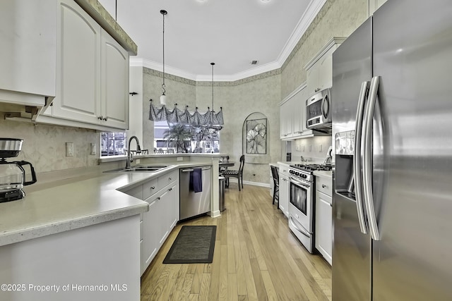 kitchen featuring pendant lighting, white cabinetry, stainless steel appliances, sink, and light hardwood / wood-style flooring