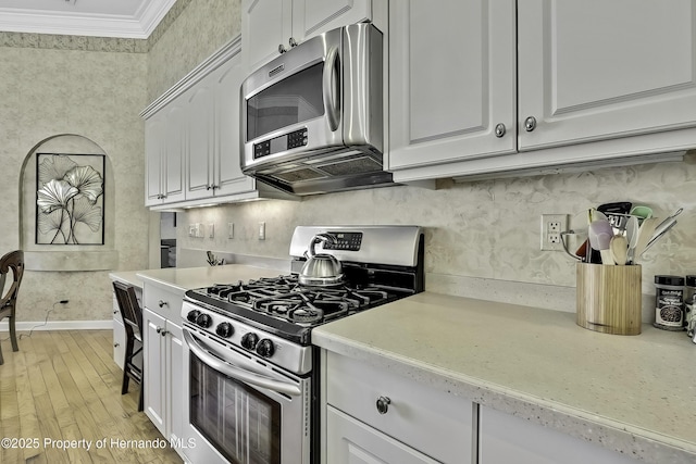 kitchen featuring tasteful backsplash, light hardwood / wood-style floors, appliances with stainless steel finishes, ornamental molding, and white cabinets