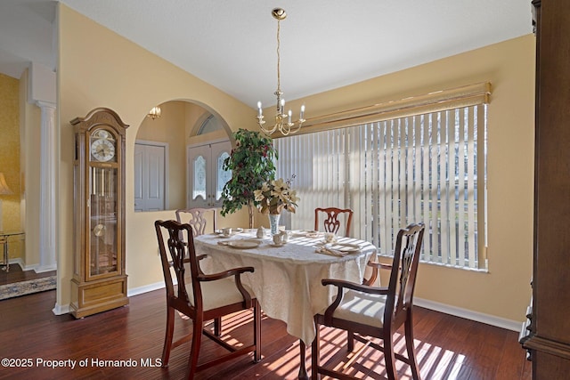 dining area with dark wood-type flooring, a chandelier, and vaulted ceiling