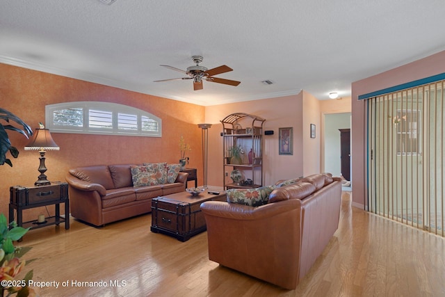 living room with ceiling fan, ornamental molding, a textured ceiling, and light hardwood / wood-style floors