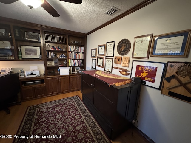 office with a textured ceiling, ceiling fan, visible vents, light wood-style floors, and ornamental molding