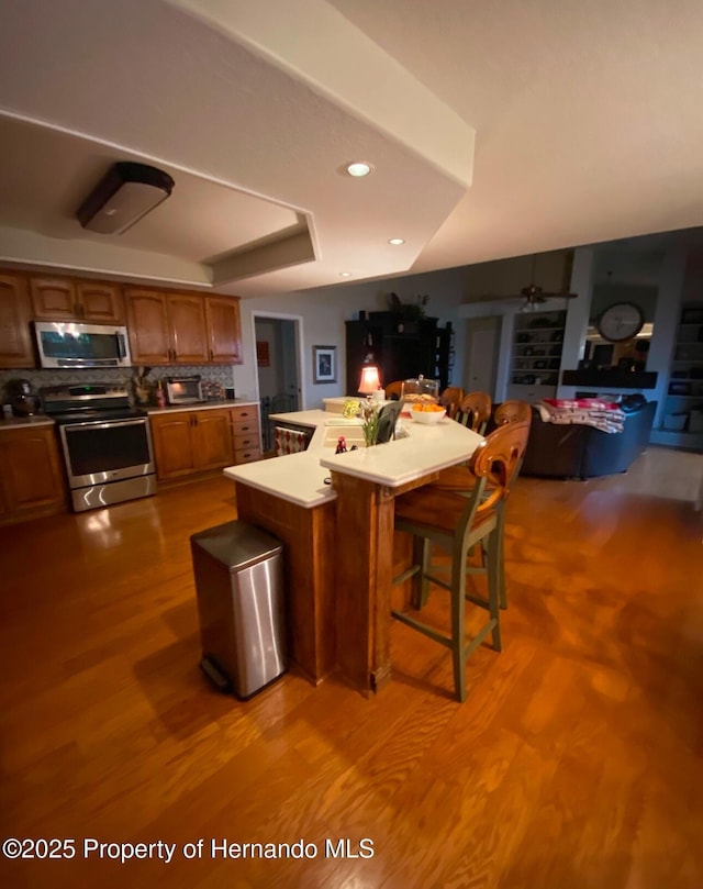 kitchen with a kitchen bar, appliances with stainless steel finishes, a kitchen island, hardwood / wood-style flooring, and backsplash