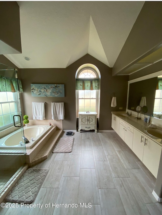 bathroom featuring lofted ceiling, vanity, and tiled bath