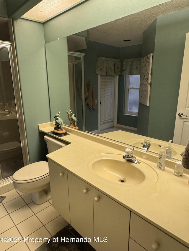 bathroom featuring tile patterned flooring, vanity, walk in shower, toilet, and a textured ceiling