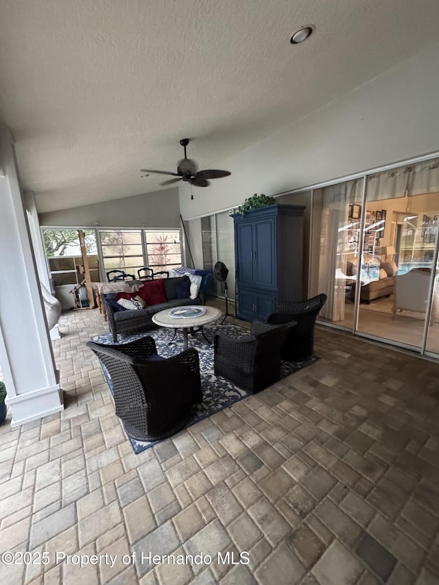 living room with ceiling fan, vaulted ceiling, and a textured ceiling