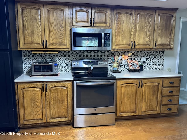 kitchen with tasteful backsplash, appliances with stainless steel finishes, and light wood-type flooring