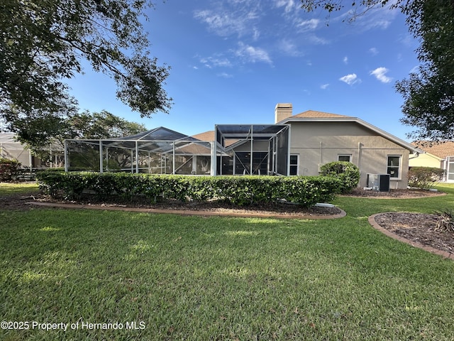 rear view of property featuring a lanai, central air condition unit, a yard, stucco siding, and a chimney