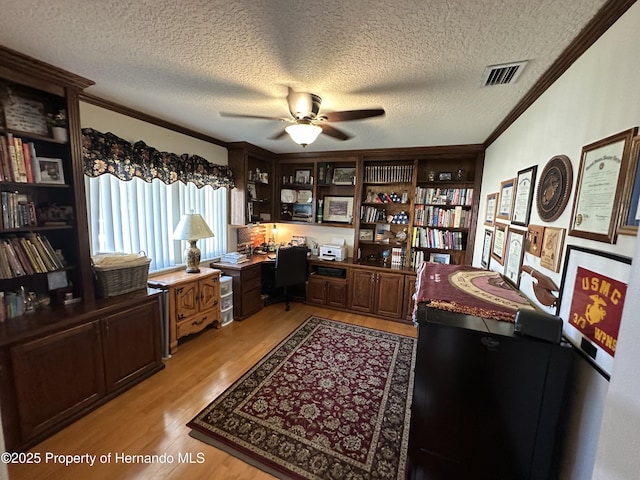 office featuring ceiling fan, visible vents, light wood-type flooring, built in study area, and crown molding