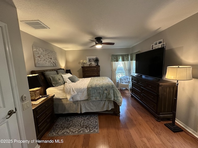 bedroom with dark wood-type flooring, visible vents, ceiling fan, and baseboards