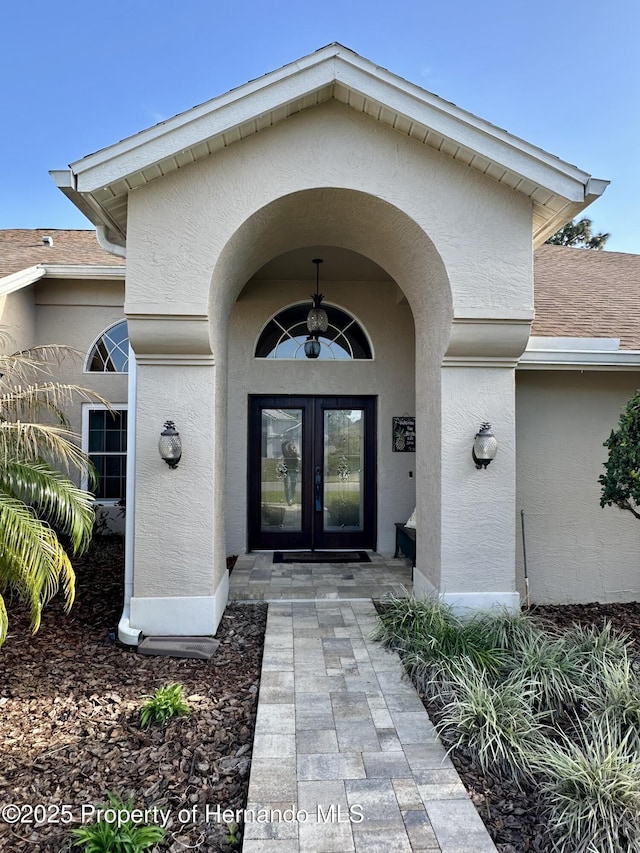 view of exterior entry featuring roof with shingles, french doors, and stucco siding