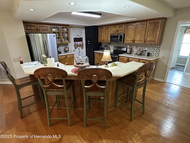 kitchen with appliances with stainless steel finishes, a kitchen bar, wood finished floors, and decorative backsplash