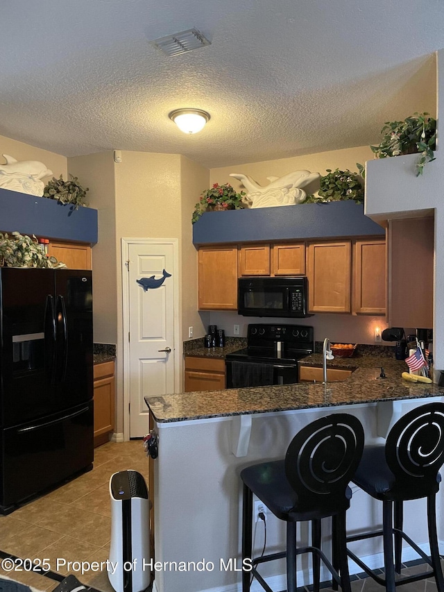 kitchen featuring black appliances, a kitchen bar, dark stone countertops, sink, and kitchen peninsula