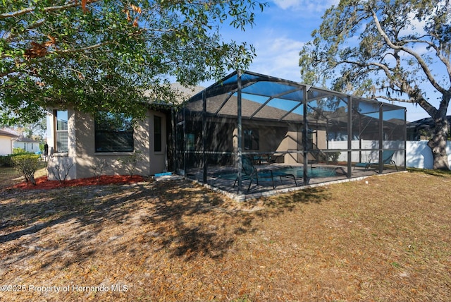 rear view of property with a lawn, a fenced in pool, a patio, glass enclosure, and stucco siding