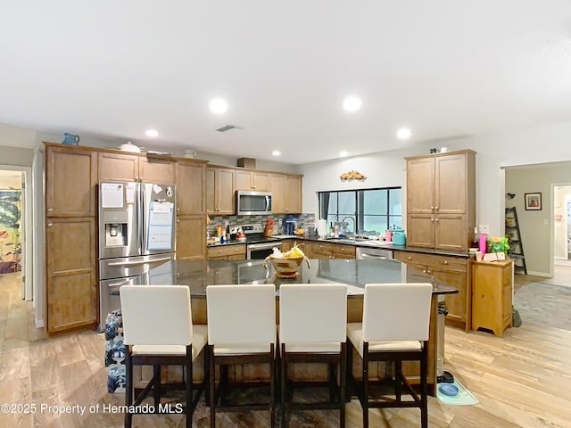 kitchen featuring appliances with stainless steel finishes, sink, backsplash, light hardwood / wood-style floors, and a breakfast bar area