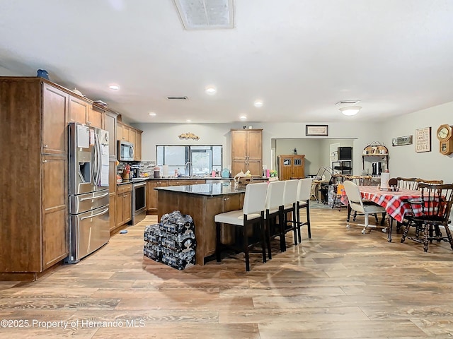 kitchen featuring appliances with stainless steel finishes, a kitchen island, tasteful backsplash, light hardwood / wood-style floors, and a breakfast bar