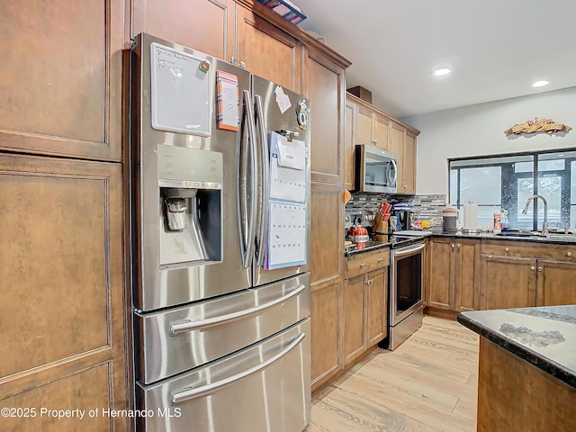 kitchen with light hardwood / wood-style floors, tasteful backsplash, sink, dark stone countertops, and stainless steel appliances