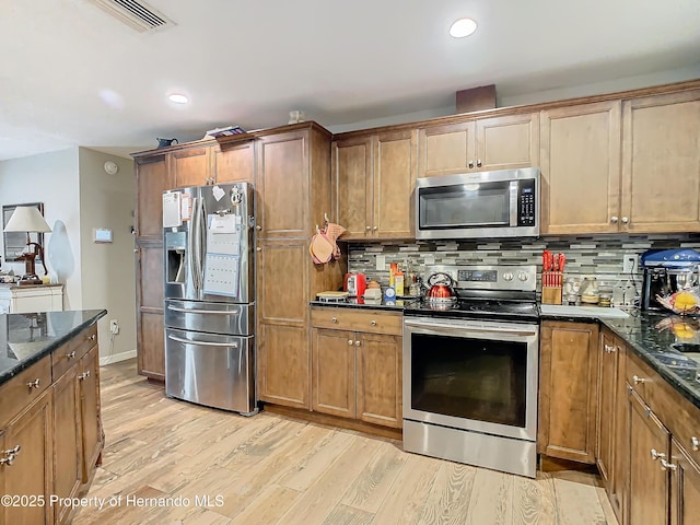 kitchen featuring light wood-type flooring, dark stone countertops, appliances with stainless steel finishes, and tasteful backsplash