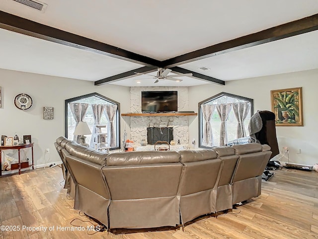 living room featuring ceiling fan, a stone fireplace, light hardwood / wood-style floors, and lofted ceiling with beams