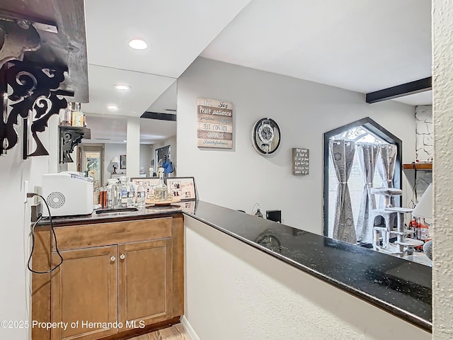 kitchen featuring sink, kitchen peninsula, beamed ceiling, and dark stone countertops