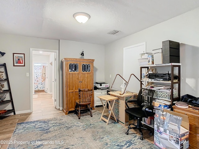 home office featuring light wood-type flooring and a textured ceiling