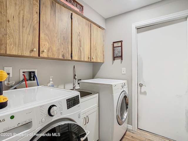 clothes washing area with light hardwood / wood-style floors, cabinets, sink, and washing machine and clothes dryer