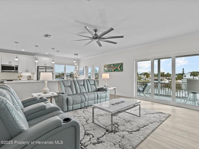 living room featuring ceiling fan, ornamental molding, a water view, and light hardwood / wood-style flooring