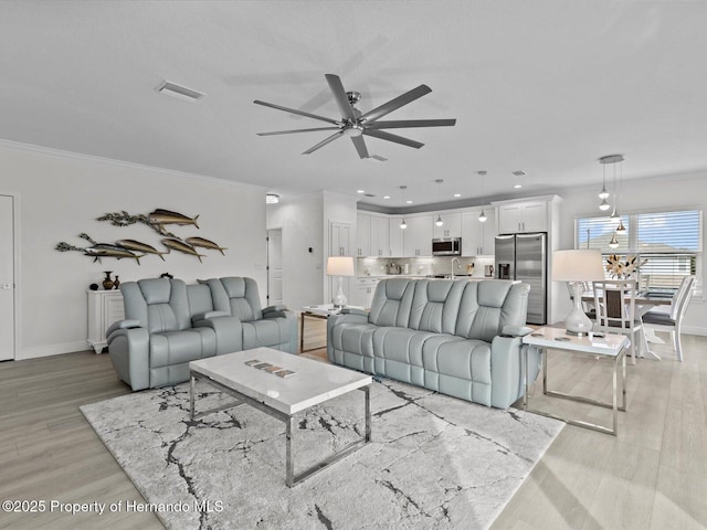 living room featuring ceiling fan, light wood-type flooring, sink, and crown molding