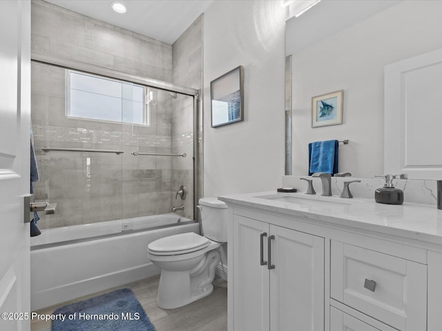 full bathroom with toilet, combined bath / shower with glass door, wood-type flooring, and vanity