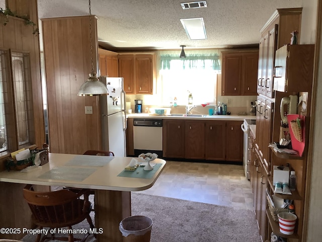 kitchen with decorative light fixtures, sink, a breakfast bar area, white appliances, and a textured ceiling