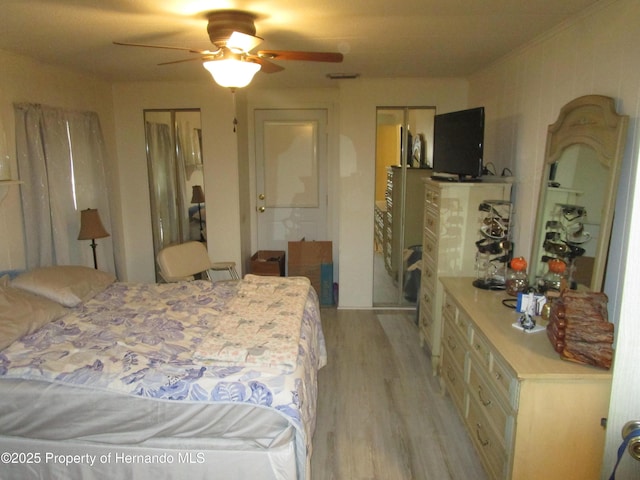 bedroom with ceiling fan, two closets, and light hardwood / wood-style flooring