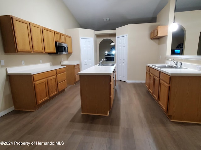 kitchen with hanging light fixtures, a kitchen island with sink, dark wood-type flooring, and sink