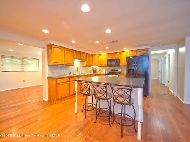 kitchen with black appliances, a center island, sink, light hardwood / wood-style flooring, and a breakfast bar