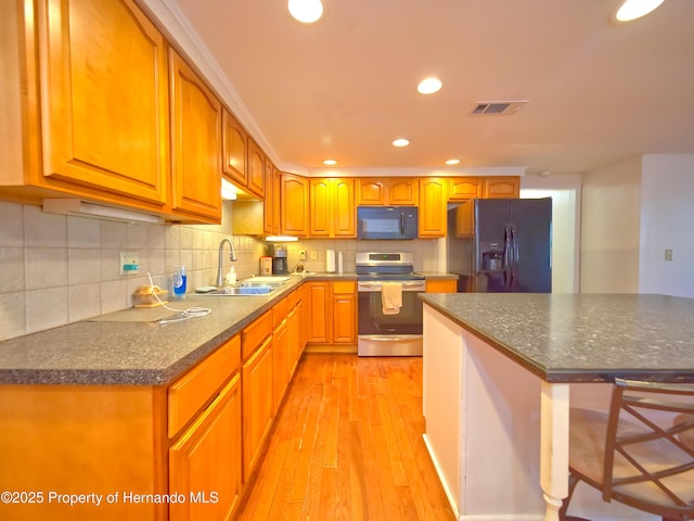 kitchen with black appliances, light hardwood / wood-style floors, decorative backsplash, sink, and a breakfast bar