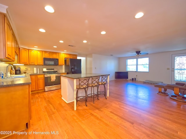 kitchen with black appliances, a kitchen island, sink, light hardwood / wood-style flooring, and a breakfast bar area