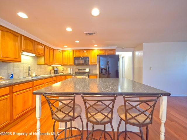 kitchen with black appliances, a kitchen island, light wood-type flooring, and a kitchen breakfast bar