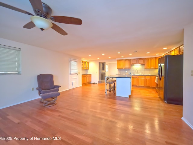 kitchen featuring black fridge, light hardwood / wood-style flooring, a center island, a breakfast bar, and decorative backsplash