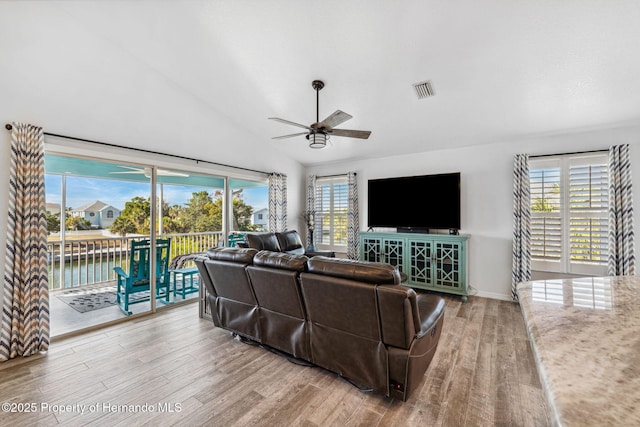 living room with ceiling fan, a water view, lofted ceiling, and light wood-type flooring