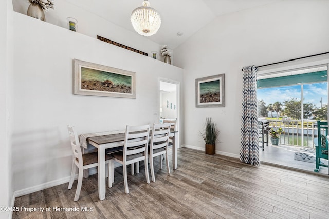 dining area with a water view, wood-type flooring, vaulted ceiling, and an inviting chandelier