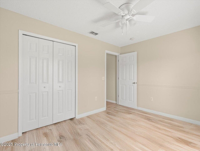 unfurnished bedroom featuring ceiling fan, a textured ceiling, a closet, and light wood-type flooring