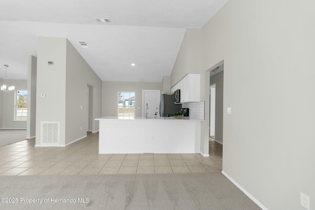 kitchen featuring white cabinets, vaulted ceiling, stainless steel refrigerator, and light colored carpet