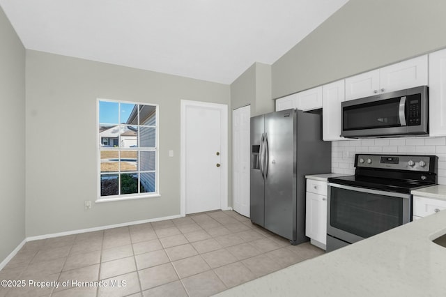 kitchen with white cabinets, appliances with stainless steel finishes, decorative backsplash, vaulted ceiling, and light tile patterned floors