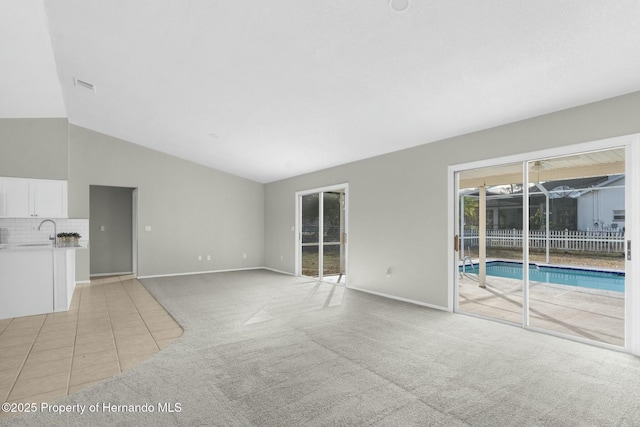 unfurnished living room featuring light colored carpet, sink, and vaulted ceiling